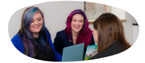 Group of three women sitting down around a laptop.