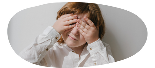 Young girl with red hair, wearing a white shirt with her hands over her eyes