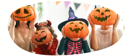 Four people holding carved pumpkins with carved faces in front of their heads. Three are children in Halloween costumes and one is an adult.