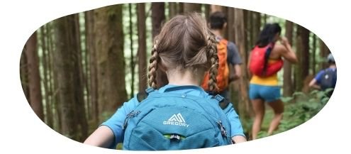 Girl with plaited hair and a light blue back pack in the woods with parents