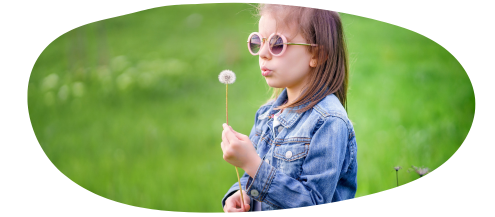 Girl blowing a dandelion in a denim jacket with sunglasses on