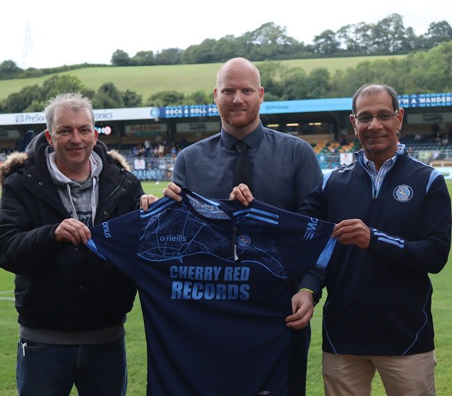 Des Mackin (Buckinghamshire Foster Carer), Mark Fawkes (Head of Fundraising and Communications, Wycombe Wanderers) and Cllr Arif Hussain (Chairman of the High Wycombe Community Board and Deputy Cabinet Member for Communities) holding a football shirt at Wycombe Wanderers.