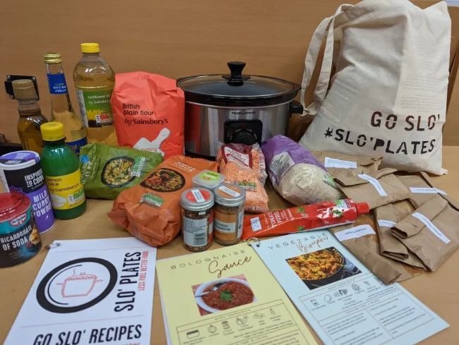 A slow cooker, pantry essentials and recipe cards spread out on a wooden table